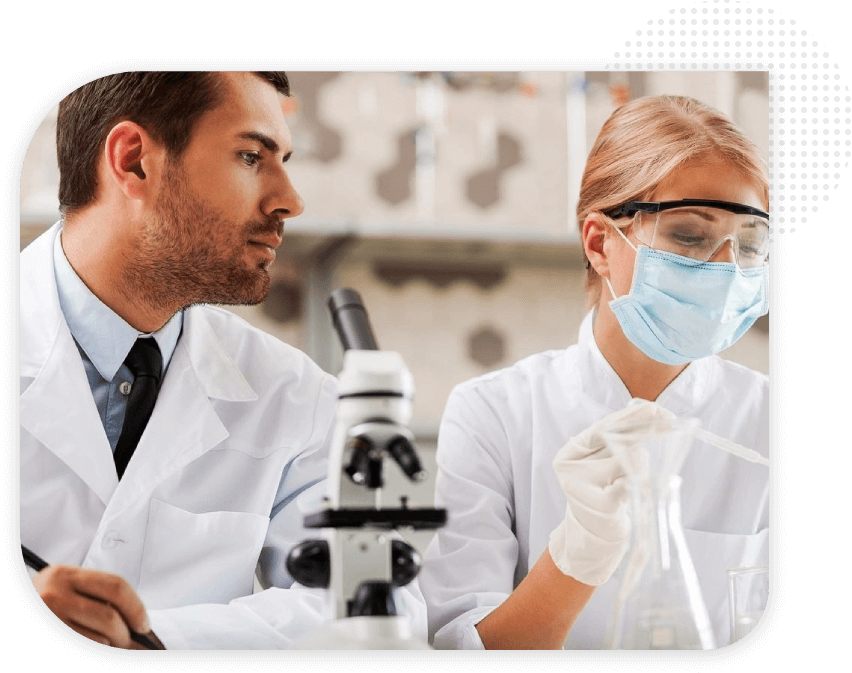 Two people in lab coats and masks looking at a microscope.